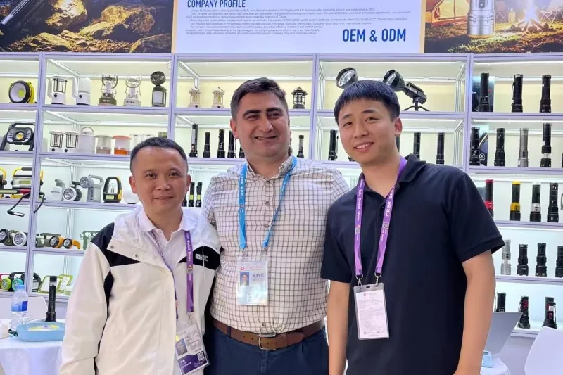 PLD staff and a buyer standing in front of the OEM and ODM product wall at a lighting exhibition